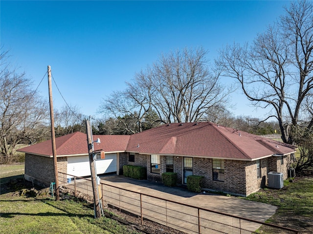 view of front of home with driveway, a fenced front yard, a garage, brick siding, and central AC unit