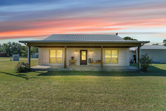 back of property at dusk with a patio, a yard, brick siding, and metal roof