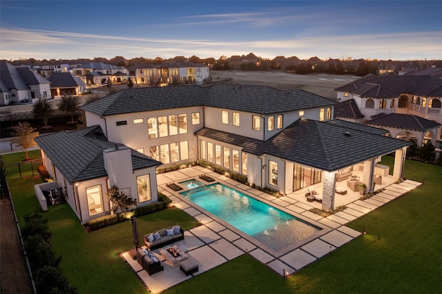 back of property at dusk featuring a yard, a patio area, a residential view, and stucco siding