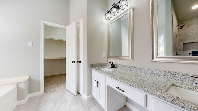 bathroom with double vanity, a spacious closet, tiled shower, and a sink