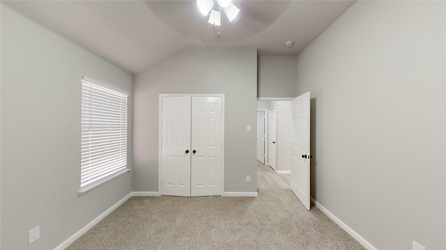 unfurnished bedroom with baseboards, lofted ceiling, ceiling fan, a closet, and light carpet