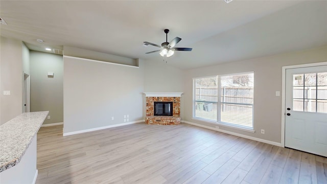 unfurnished living room featuring plenty of natural light, a fireplace, a ceiling fan, and light wood-style floors