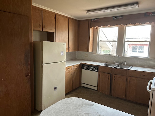 kitchen featuring white appliances, brown cabinetry, a sink, light countertops, and dark floors