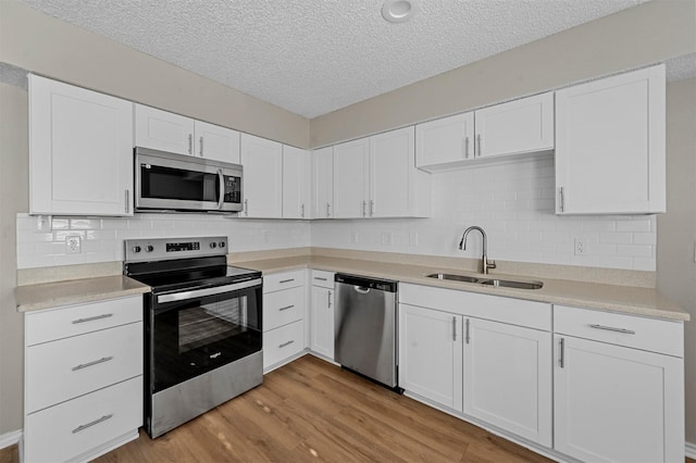 kitchen featuring light wood-style flooring, a sink, light countertops, white cabinets, and appliances with stainless steel finishes