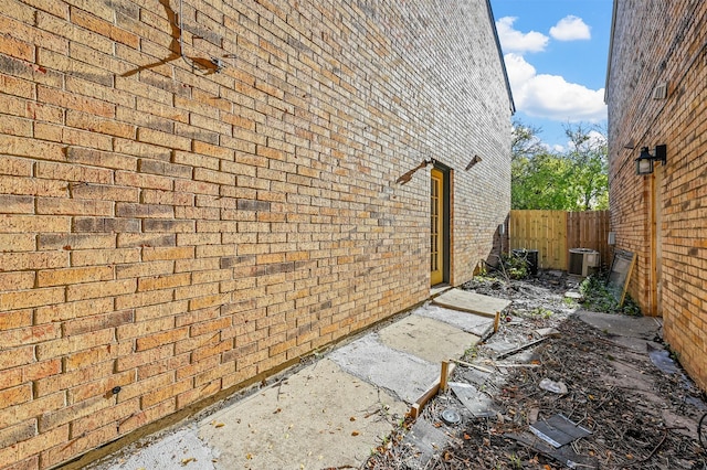 view of home's exterior with cooling unit, fence, and brick siding