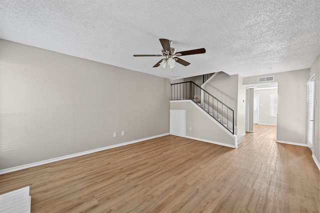 unfurnished living room with visible vents, baseboards, stairway, light wood-style flooring, and a textured ceiling