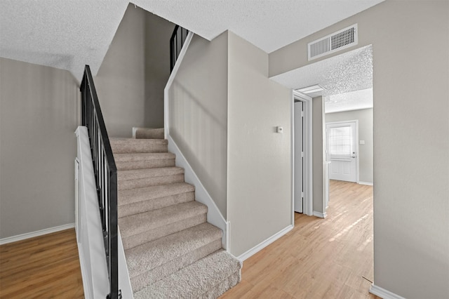 staircase with baseboards, wood finished floors, visible vents, and a textured ceiling