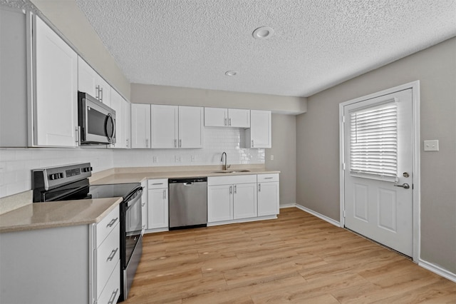 kitchen with a sink, stainless steel appliances, light countertops, light wood-style floors, and white cabinetry