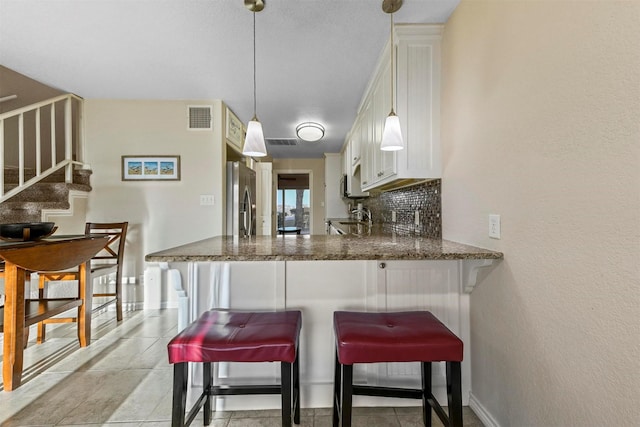 kitchen featuring a breakfast bar area, visible vents, a peninsula, stainless steel fridge with ice dispenser, and decorative backsplash