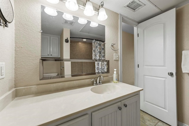 full bathroom featuring vanity, curtained shower, a textured wall, and visible vents