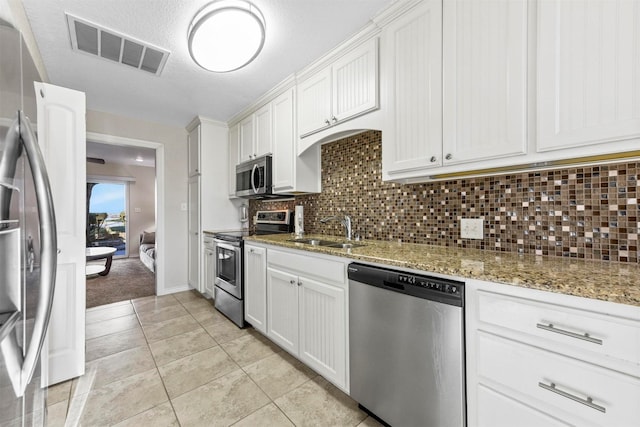 kitchen featuring visible vents, light stone counters, stainless steel appliances, white cabinetry, and a sink