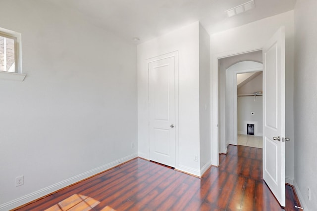 bedroom with arched walkways, visible vents, baseboards, and wood finished floors