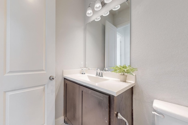 bathroom with toilet, vanity, and a textured wall