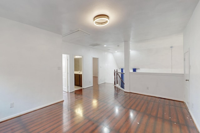 empty room with visible vents, baseboards, attic access, and wood finished floors