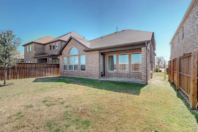 back of house featuring a yard, a fenced backyard, brick siding, and a shingled roof