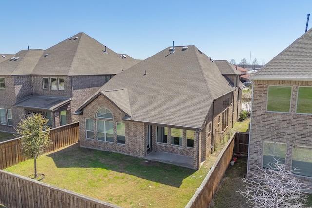 rear view of property with brick siding, a shingled roof, a lawn, a fenced backyard, and a patio area