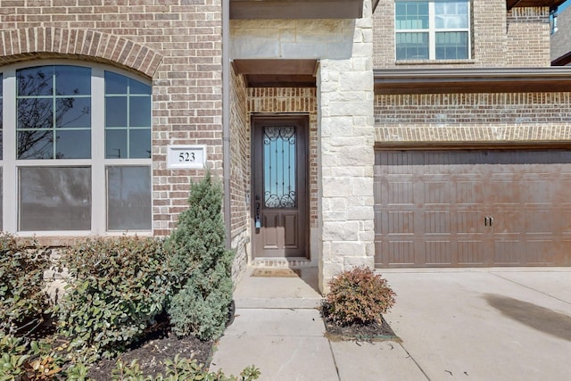 doorway to property featuring a garage, brick siding, and driveway