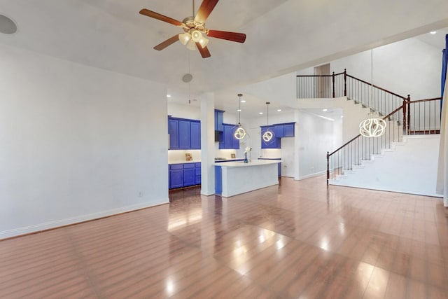 unfurnished living room featuring stairway, wood finished floors, baseboards, a high ceiling, and ceiling fan