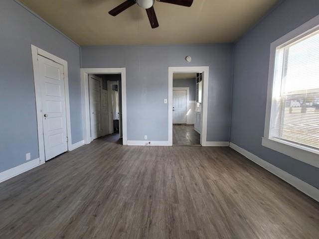 unfurnished bedroom featuring ceiling fan, ensuite bath, baseboards, and dark wood-style flooring