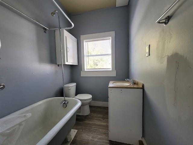 bathroom featuring baseboards, toilet, a freestanding tub, wood finished floors, and vanity