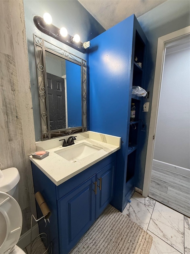 bathroom featuring vanity, toilet, baseboards, and marble finish floor