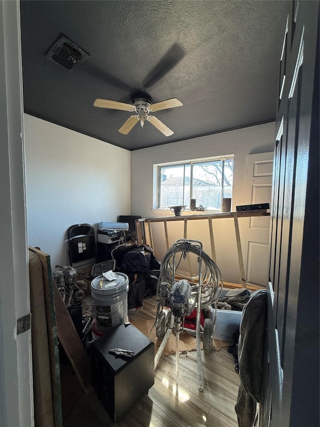 interior space with ceiling fan, visible vents, a textured ceiling, and wood finished floors