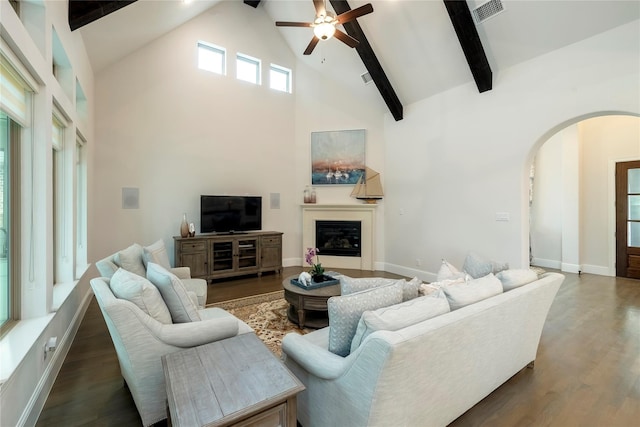 living room with beam ceiling, wood finished floors, arched walkways, a glass covered fireplace, and high vaulted ceiling