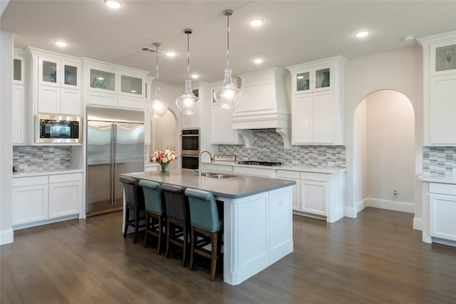 kitchen with premium range hood, a kitchen bar, a sink, arched walkways, and built in appliances