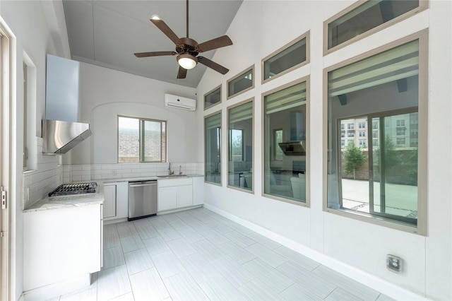 kitchen with a wall mounted air conditioner, a sink, appliances with stainless steel finishes, wall chimney exhaust hood, and decorative backsplash