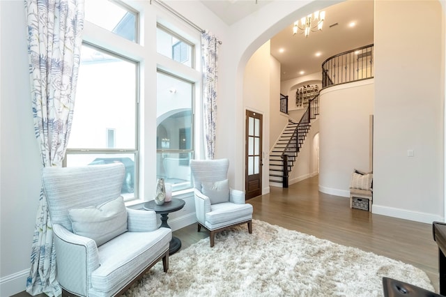 sitting room with stairway, wood finished floors, baseboards, arched walkways, and a notable chandelier