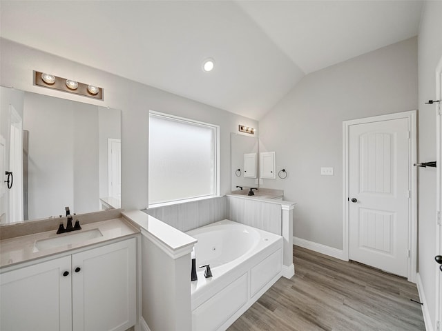 full bathroom featuring a garden tub, two vanities, a sink, wood finished floors, and lofted ceiling