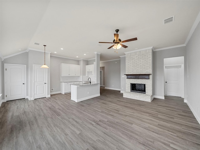 unfurnished living room featuring baseboards, light wood finished floors, a sink, ceiling fan, and a brick fireplace