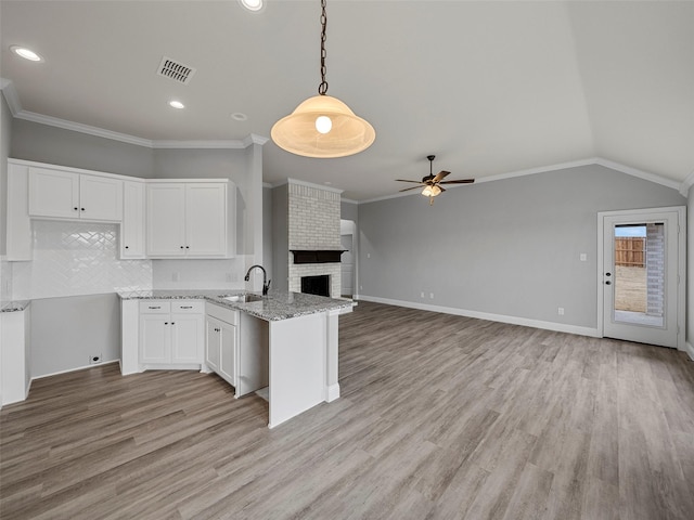 kitchen featuring visible vents, a sink, open floor plan, white cabinetry, and a peninsula