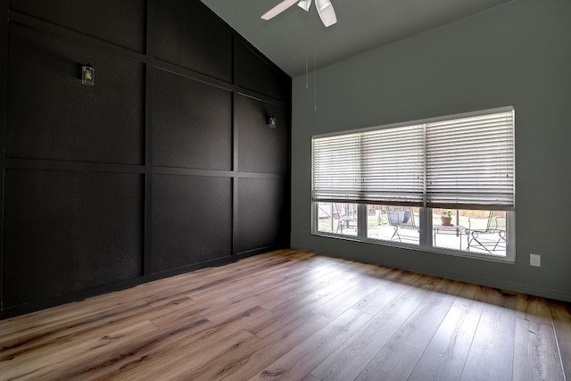 spare room featuring lofted ceiling, a decorative wall, light wood finished floors, and ceiling fan