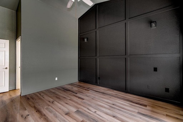 unfurnished bedroom with lofted ceiling, light wood-style flooring, and a decorative wall