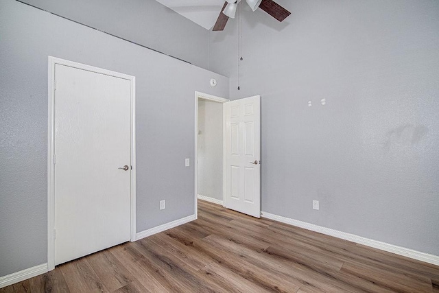 unfurnished bedroom featuring a ceiling fan, wood finished floors, baseboards, and a towering ceiling