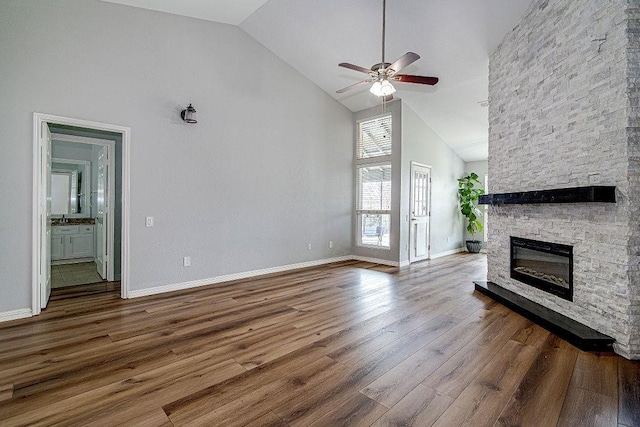 unfurnished living room featuring a ceiling fan, wood finished floors, baseboards, high vaulted ceiling, and a fireplace