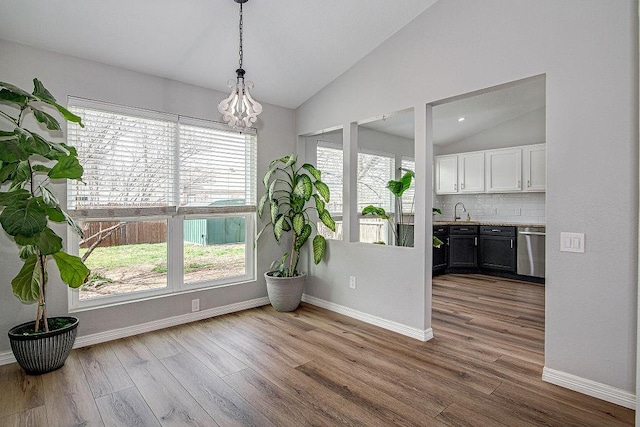 unfurnished dining area featuring a sink, baseboards, lofted ceiling, and dark wood finished floors