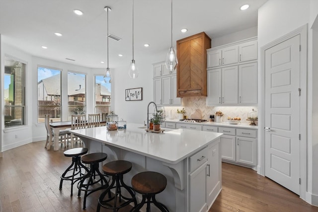 kitchen featuring visible vents, a center island with sink, stainless steel gas cooktop, wood-type flooring, and tasteful backsplash