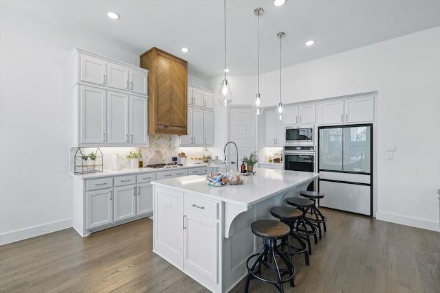 kitchen featuring an island with sink, light countertops, decorative backsplash, stainless steel appliances, and white cabinetry