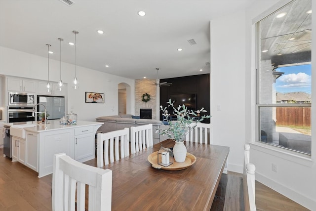 dining room featuring baseboards, recessed lighting, a fireplace, light wood-style floors, and arched walkways