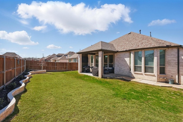 back of property featuring brick siding, roof with shingles, a fenced backyard, a yard, and a patio