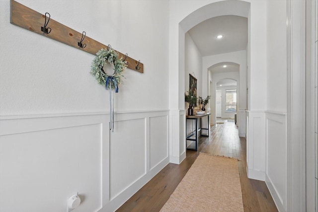 hallway with a decorative wall, dark wood-style floors, arched walkways, and wainscoting