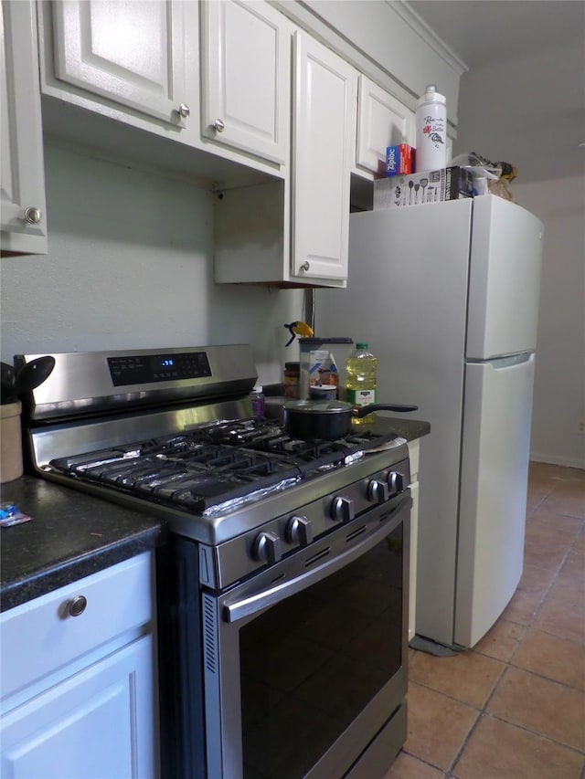 kitchen with dark countertops, white cabinets, light tile patterned flooring, and stainless steel gas range oven