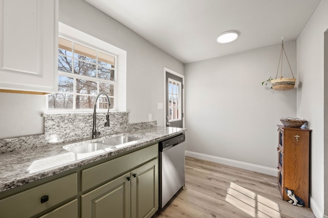 kitchen with green cabinets, light wood-type flooring, light stone counters, dishwasher, and a sink