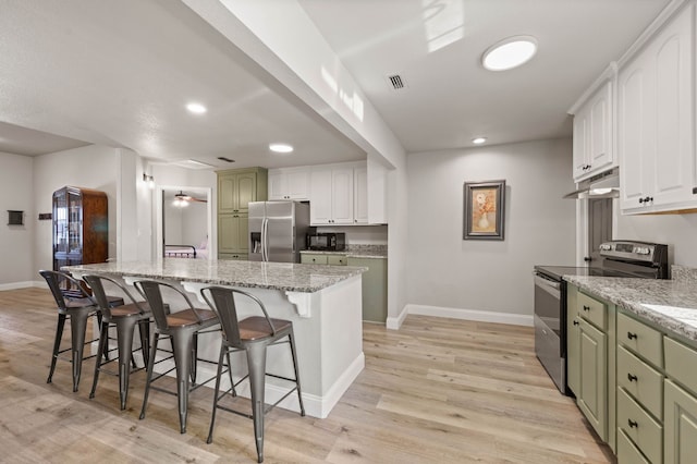 kitchen featuring a kitchen breakfast bar, appliances with stainless steel finishes, baseboards, under cabinet range hood, and visible vents