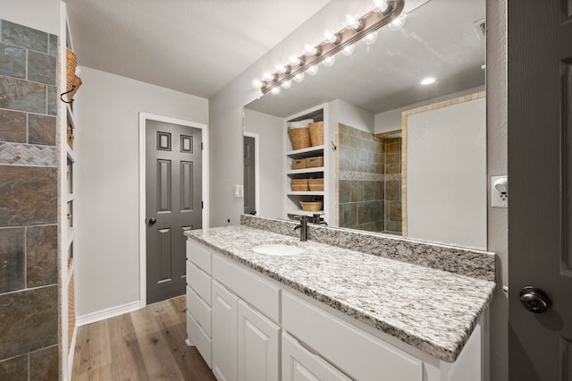 bathroom featuring baseboards, wood finished floors, vanity, and a tile shower