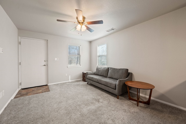 carpeted living area with ceiling fan, baseboards, and visible vents