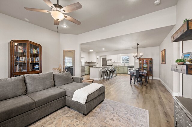 living area featuring ceiling fan with notable chandelier, baseboards, recessed lighting, and light wood-style floors