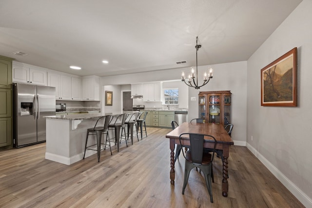 dining room featuring an inviting chandelier, light wood-style floors, visible vents, and baseboards